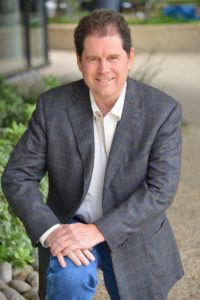 David Munson kneeling, wearing sport coat and jeans.