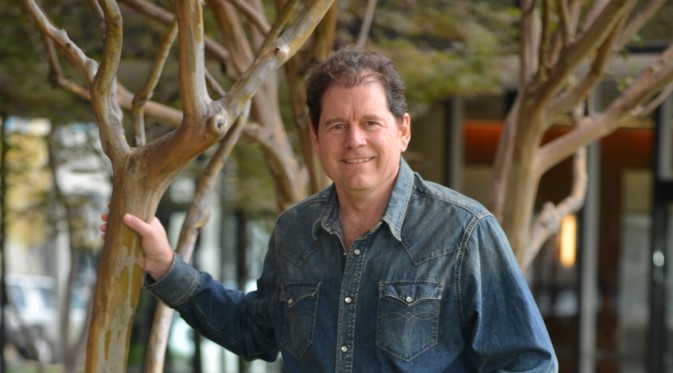 David Munson leaning on a tree, wearing denim shirt.
