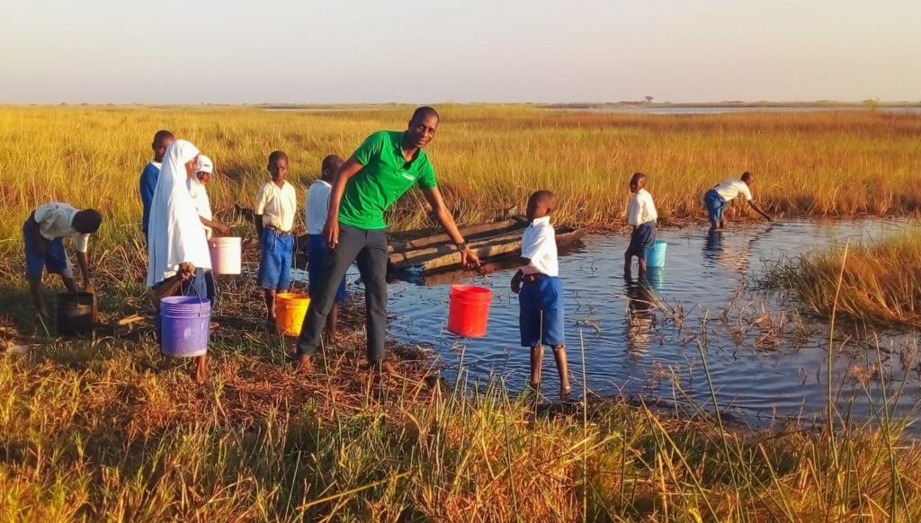 David Paul and several children collecting water in buckets from a lake.