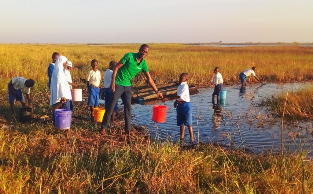 David Paul and several children collecting water in buckets from a lake.