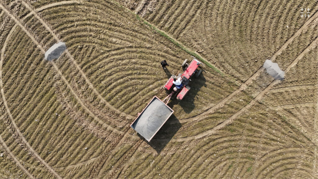 Tractor pulling trailer of rock dust in plowed field